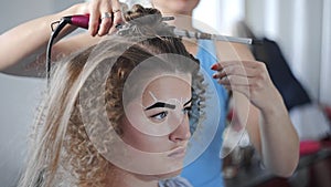 Stylist makes curly afro hairstyle for woman by hot curling hair, process of making hairstyle, hairstyles in the beauty