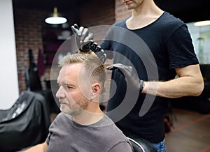 Stylist making hairstyle for person in barbershop. Hairdresser is cutting hair of handsome bearded mature man in salon. Services