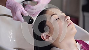 Stylist washing client`s hair in sink in beauty salon