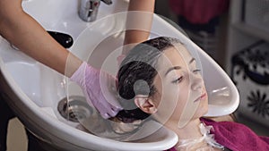 Stylist washing client`s hair in sink in beauty salon