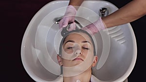 Stylist washing client`s hair in sink in beauty salon