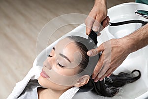 Stylist washing client`s hair at sink in beauty salon