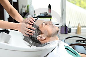 Stylist washing client`s hair at sink in salon