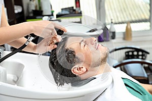 Stylist washing client`s hair at sink in salon