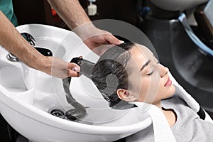 Stylist washing client`s hair at sink in salon