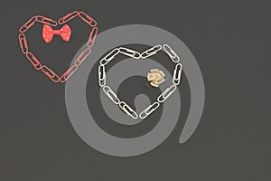 Stylized hearts from red and white stationery clips with red bow tie and satin pastel color flower on dark background. Minimalism