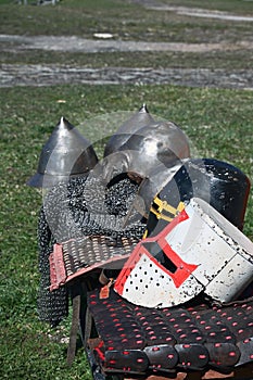 Stylized metal helmets of ancient Russian warriors and Livonia knights lie in a row on metal and leather armor.
