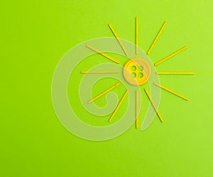 Stylized Yellow sun made from button and wood sticks on a green background.