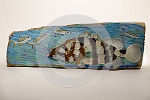 A stylizeed Carribean Grouper made from cut sea glass and mounted on a blue painted piece of driftwood