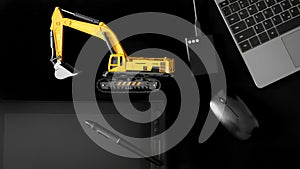 Stylus and graphics tablet with interactive screen, mouse, laptop and usb ssd on black background next to yellow excavator model.