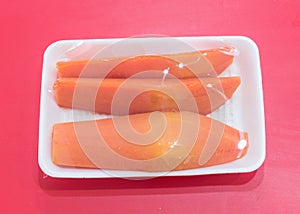 Styrofoam tray packed with sliced papaya in transparent food film wrap on red table at Asian market