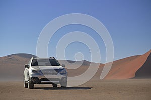 Subaru Outback stands in the middle of the Namib Desert, next to a sand dune of Sossusvlei.