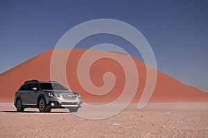 Subaru Outback stands in the middle of the Namib Desert, next to a sand dune of Sossusvlei.