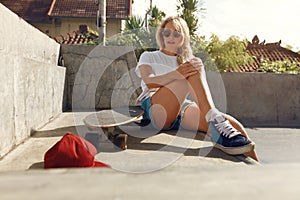 Subculture. Skater Girl Sitting On Concrete Ramp At Skatepark. Teenager In Casual Outfit Posing Outdoor. photo