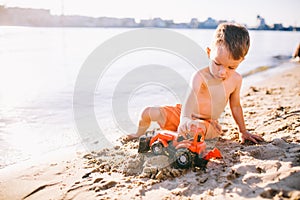 Subject construction and heavy industry. Abstraction child boy playing on the sand near the river in the summer toy red tractor