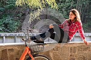 Subject ecological bicycle transport. A young caucasian woman in jeans and a shirt student sits resting in a park near the lake