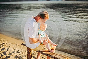 Subject recreation father and little son. Young caucasian dad sits on wooden bench overlooking the town Kiev and holding river of