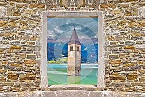 Submerged bell Tower of Curon Venosta or Graun im Vinschgau on Lake Reschen landscape view through stone wall gate