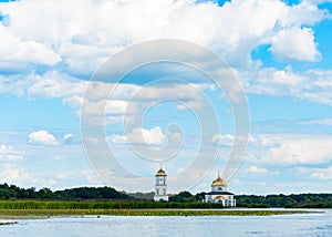 Submerged Orthodox Church surrounded by water, trees and reeds under blue sky