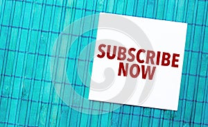 subscribe now word on torn paper with blue wooden background.