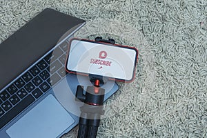 Subscribe to the Internet channel on the smartphone display on a flexible tripod with Laptop against the background of the carpet