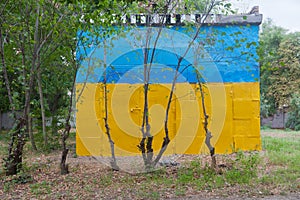 Subsidiary building painted in colors of the Ukrainian flag behind young trees