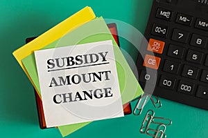 SUBSIDY ISSUE CHANGE - words on note paper against the background of a calculator and paper clips