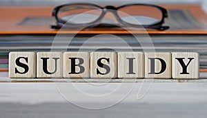SUBSIDY - word on wooden cubes on the background of a folder with documents and glasses