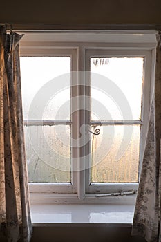 Substandard housing in England, UK, with condensation on window with curtains