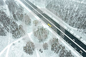 Suburb area with trees covered with fresh snow and asphalt road with cars. aerial photo