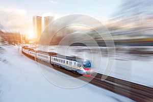 Suburban electric passenger train rushes through the snow-covered landscape of the city, motion blur effect