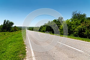 Suburban empty road asphalt surrounded by trees and grass. The concept of transportation and travel. Background green