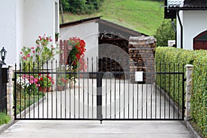 Suburban family house paved driveway closed with dark wrought iron doors mounted on stone tiles covered poles surrounded with