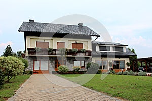 Suburban family house with stone tiles driveway and new garage surrounded with freshly cut green grass and small decorative trees