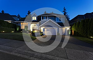 Suburban home exterior on a summer late evening with lights on yard and house