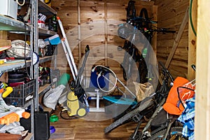 Suburban home wooden storage utility unit shed with miscellaneous stuff on shelves, bikes, exercise machine, ladder