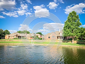 Suburban lakefront houses with water fountain and green grass lawn near Dallas