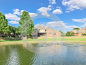 Suburban lakefront houses with water fountain and green grass lawn near Dallas