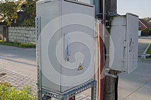 Suburban power distribution cabinets with locked doors, mounted on and near pole on metal frame with wires in corrugated pipe.