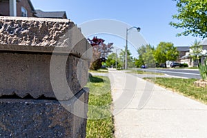 Suburban street with close up of rough beige stone pillar - decorative edge - brick houses and green lawns in background