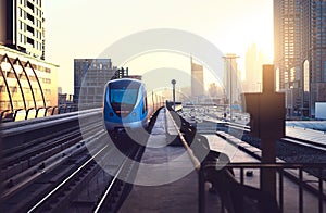 Subway train at sunset in modern city. Dubai metro. Downtown skyline with sundown. Skyscraper buildings and car traffic.