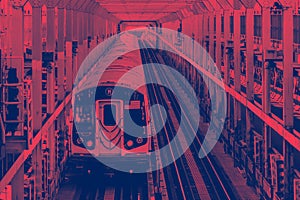 Subway train traveling on tracks across the Williamsburg Bridge from Brooklyn to Manhattan in New York City with red blue colors