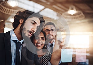 Succeeding is top priority. a group of businesspeople brainstorming with notes on a glass wall in an office.