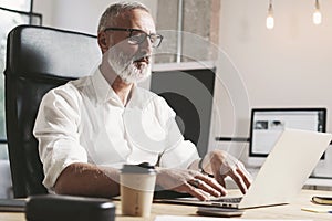 Succes and confidental adult businessman using mobile laptop computer while working at the wooden table at modern