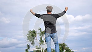 Succesful man raises hands up standing back on top of the mountain. Achievement success motivation winner concept. slow
