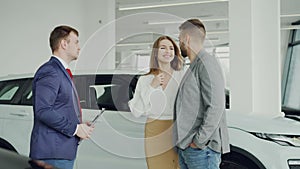 Succesful young man is buying car for his wife shaking hands with dealership agent then kissing attractive woman who is
