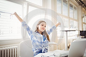 Succesfull businesswoman with arms outstretched while sitting at office