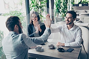 Success and agreement between three business partners, they celebrate sitting in cafe, wearing suits, smiling. Terrace is