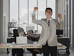 Success asian business man raised arm fist to celebrate in office