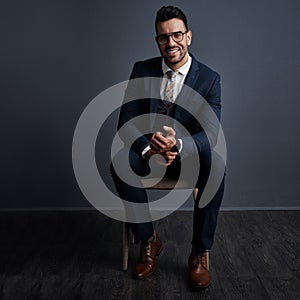 Success built on self confidence. Studio shot of a stylish young businessman sitting on a chair against a gray